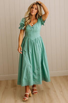 Woman wearing a teal dress standing against a beige wall.