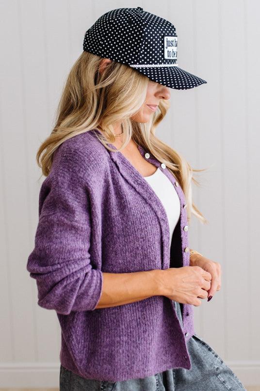 BLONDE WOMAN WEARING A COZY RIBBED TEXTURE CARDIGAN WITH SHELL BUTTONS AND A POLKA DOT HAT.