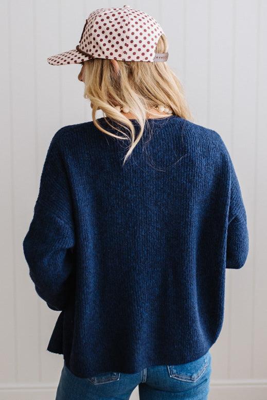 BLONDE WOMAN WEARING A COZY RIBBED TEXTURE CARDIGAN WITH SHELL BUTTONS AND A POLKA DOT HAT.