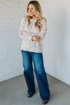 Woman wearing a floral blouse and blue jeans against a white brick wall.