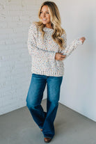 Woman wearing a patterned sweater and blue jeans against a white brick wall.