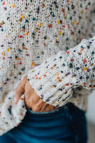 Close-up of a person wearing a textured sweater with colorful speckles.