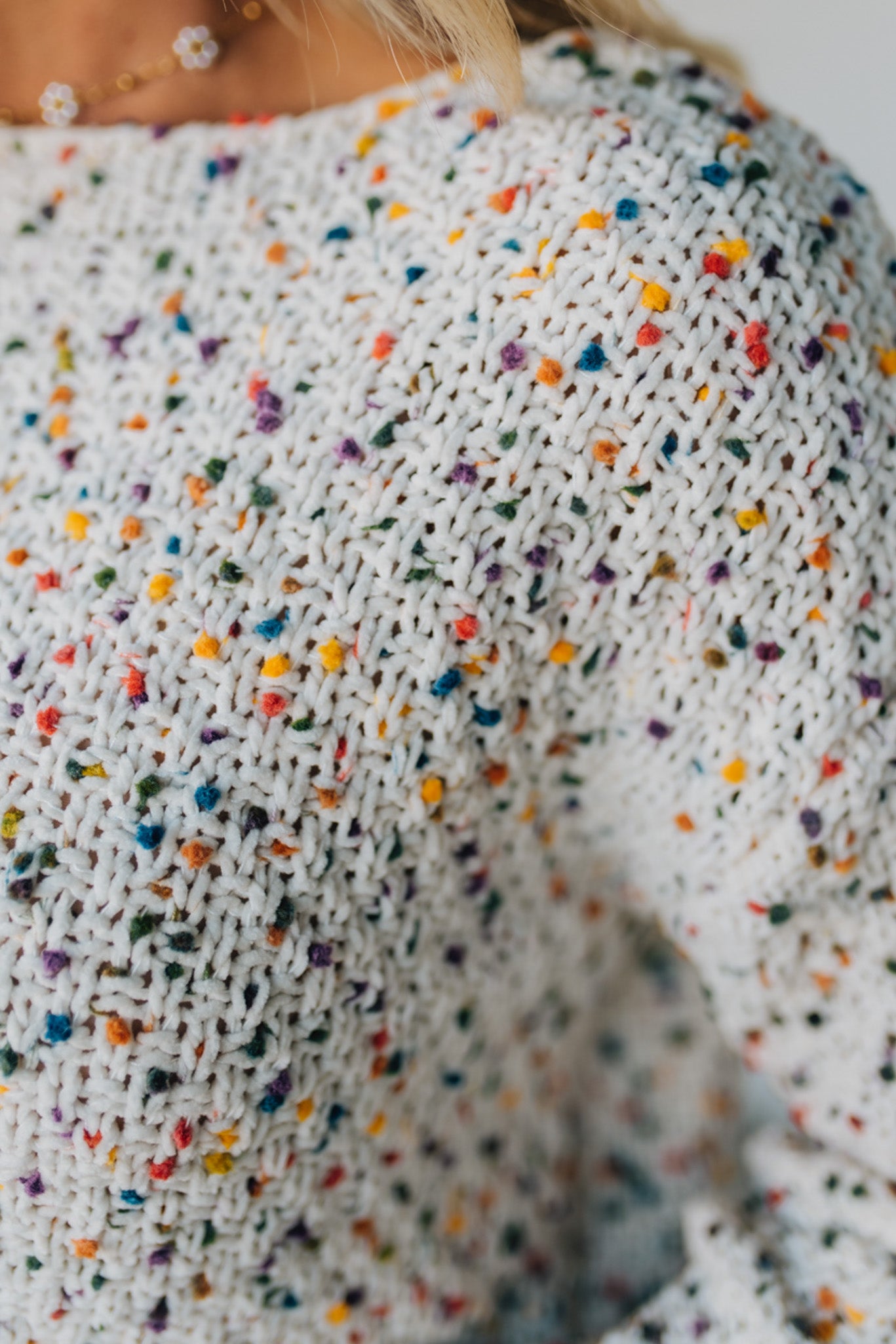 Close-up of a white knitted sweater with colorful speckles.
