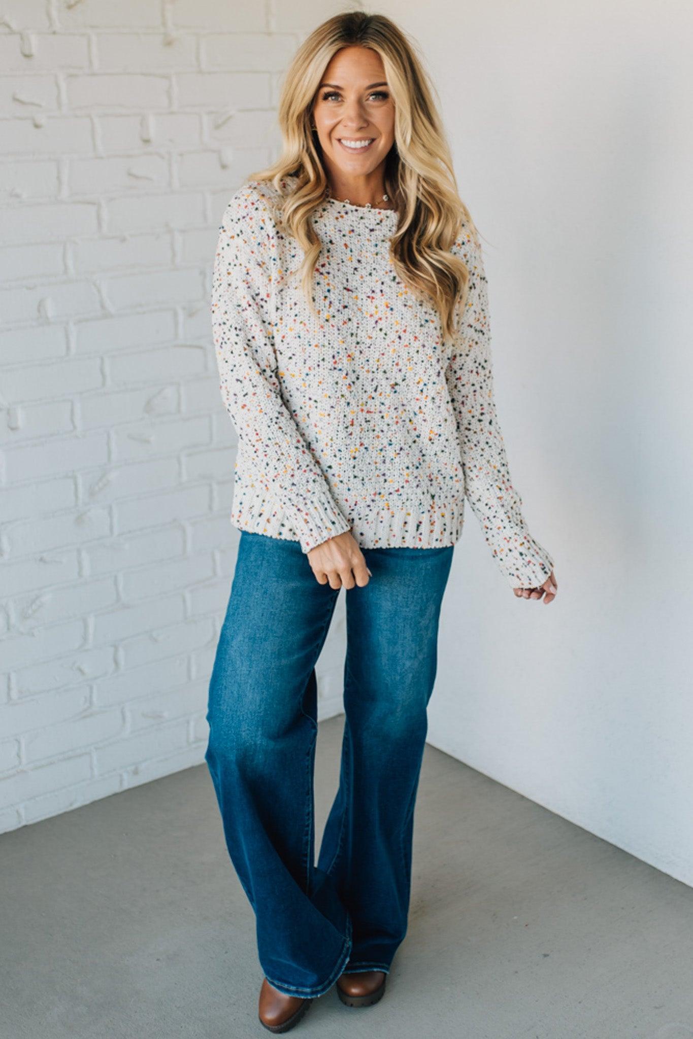 Woman wearing a floral blouse and blue jeans against a white brick wall.