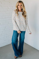 Woman wearing a floral blouse and blue jeans against a white brick wall.