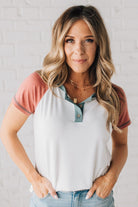 BLONDE MODEL WEARING A COLOR CONTRASTED, HALF BUTTON, SHORT SLEEVE, COLOR BLOCKED BASEBALL TOP IN FADE RED WHITE AND BLUE.