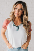 BLONDE MODEL WEARING A COLOR CONTRASTED, HALF BUTTON, SHORT SLEEVE, COLOR BLOCKED BASEBALL TOP IN FADE RED WHITE AND BLUE.