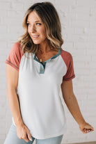 BLONDE MODEL WEARING A COLOR CONTRASTED, HALF BUTTON, SHORT SLEEVE, COLOR BLOCKED BASEBALL TOP IN FADE RED WHITE AND BLUE.