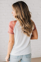 BLONDE MODEL WEARING A COLOR CONTRASTED, HALF BUTTON, SHORT SLEEVE, COLOR BLOCKED BASEBALL TOP IN FADE RED WHITE AND BLUE.