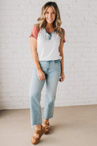 BLONDE MODEL WEARING A COLOR CONTRASTED, HALF BUTTON, SHORT SLEEVE, COLOR BLOCKED BASEBALL TOP IN FADE RED WHITE AND BLUE.