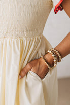 BLONDE MODEL WEARING A CREAM DRESS WITH RED CONTRASTED BINDING DETAIL AND SMOCKED BODICE MIDI DRESS WITH RUFFLE ACCENTS AND TIE BACK DETAIL.