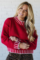Woman wearing a red sweater with white stripes against a white brick wall