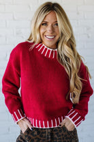 Woman wearing a red sweater with white stripes against a white brick wall.