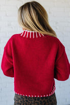 Person wearing a red sweater with white trim against a white brick wall.