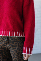 Red sweater with white trim worn by a person, with a neutral background