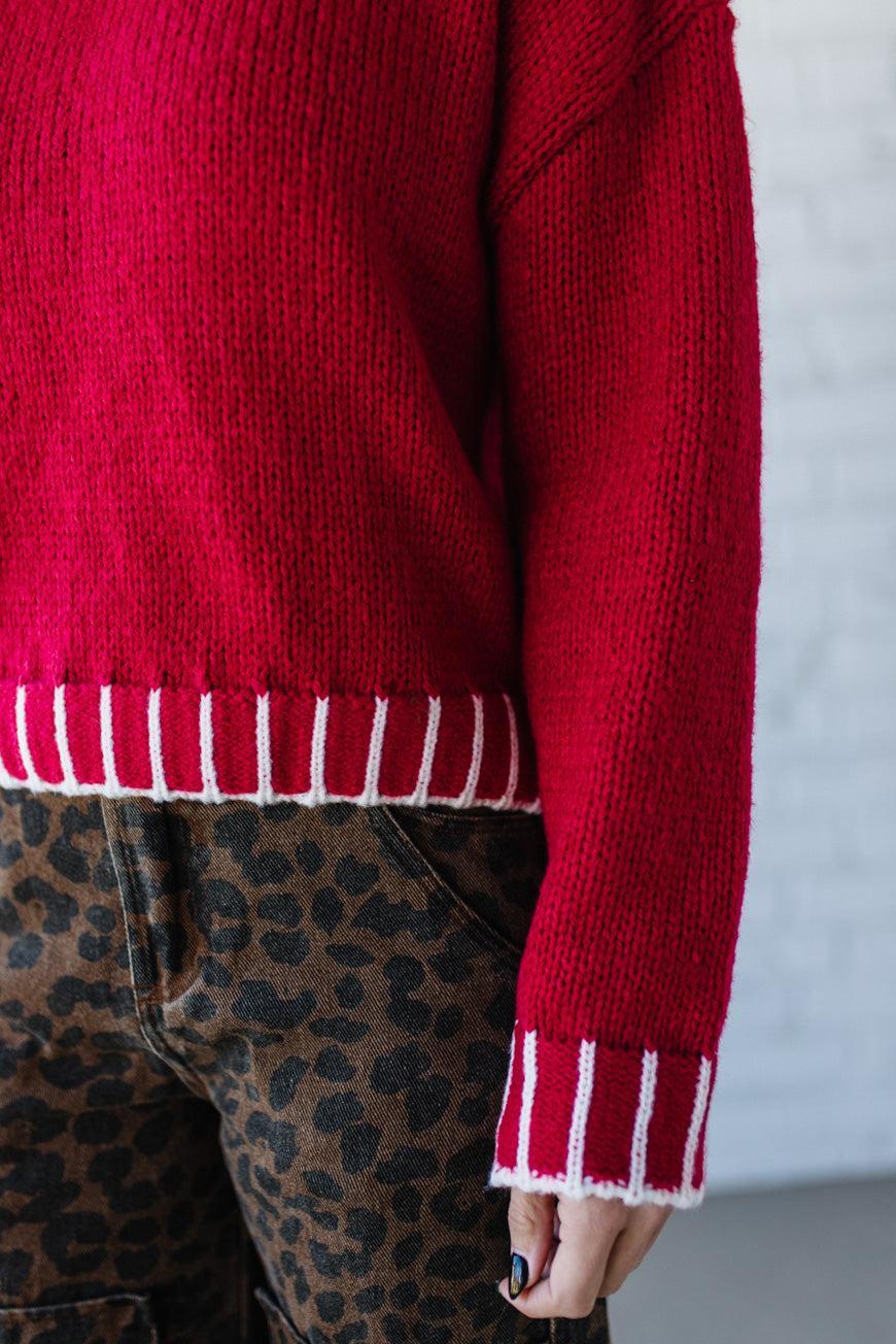 Red sweater with white trim worn by a person, with a neutral background