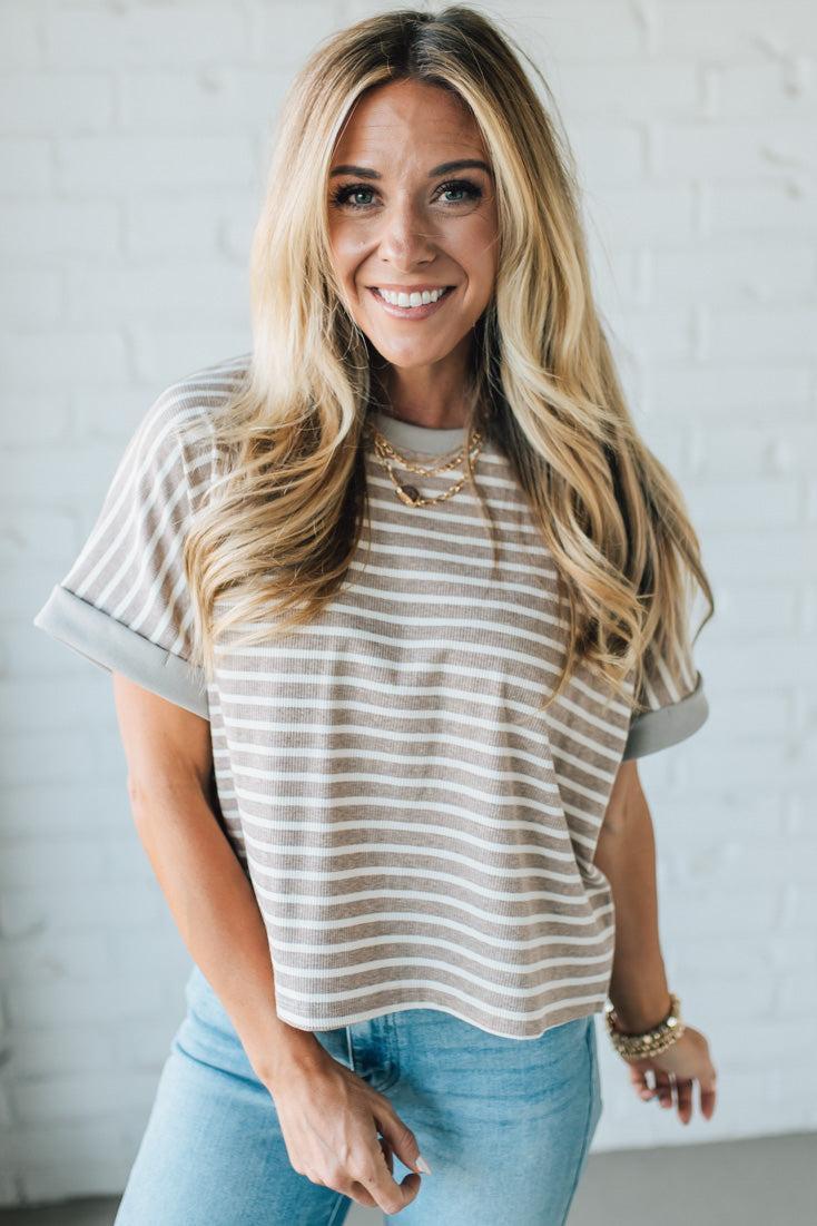Woman wearing a striped shirt and jeans against a white wall