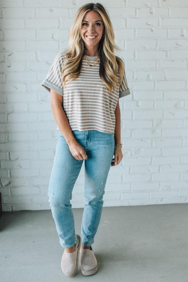Woman wearing a striped shirt and light blue jeans against a white brick wall.