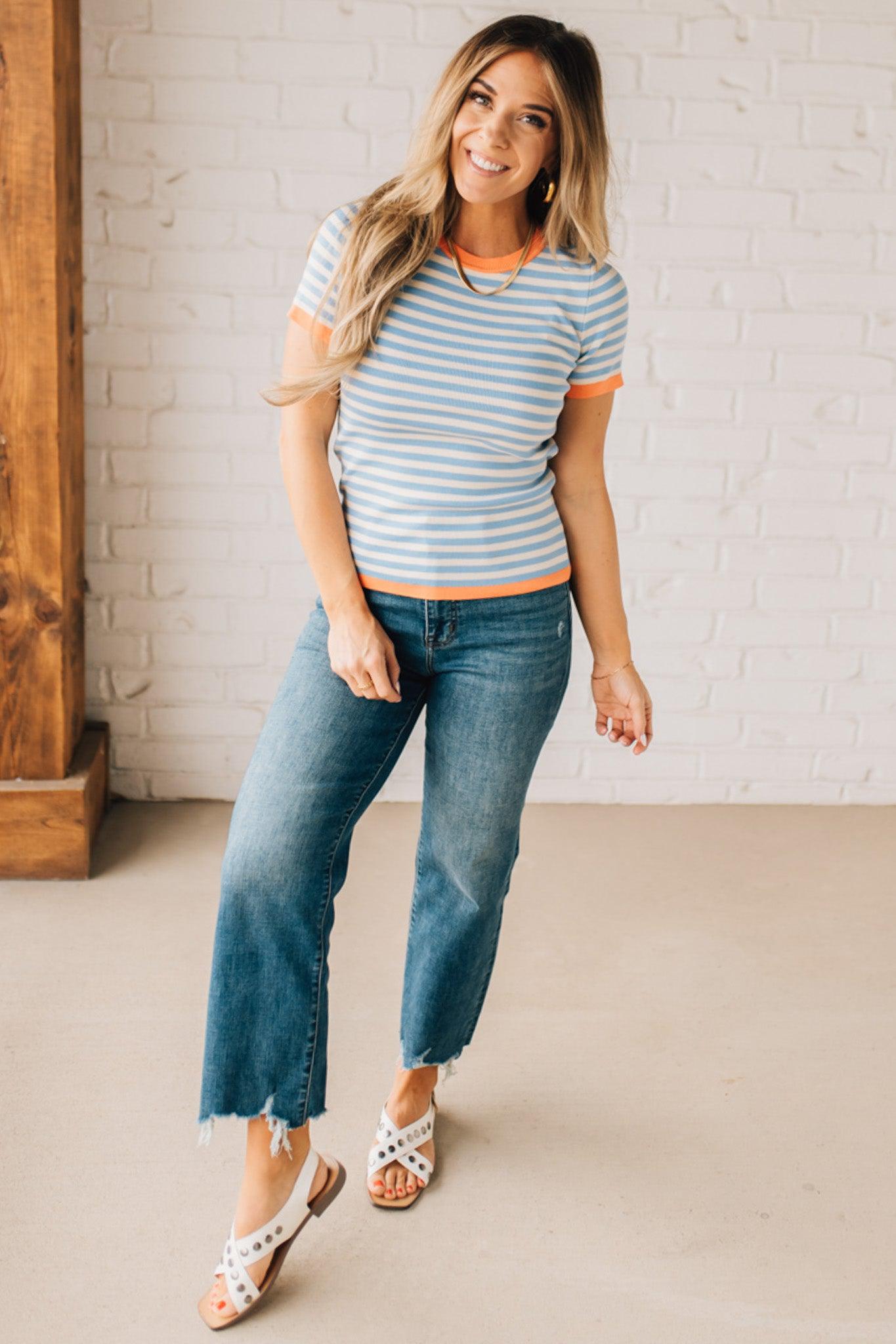 BLONDE WOMAN WEARING COLOR TRIMMED BLUE AND WHITE STRIPED SWEATER WITH SHORT SLEEVES AND BRIGHT CORAL EDGES.