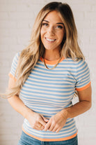 BLONDE WOMAN WEARING COLOR TRIMMED BLUE AND WHITE STRIPED SWEATER WITH SHORT SLEEVES AND BRIGHT CORAL EDGES.