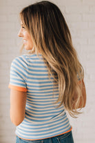 BLONDE WOMAN WEARING COLOR TRIMMED BLUE AND WHITE STRIPED SWEATER WITH SHORT SLEEVES AND BRIGHT CORAL EDGES.