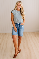 Woman wearing a striped shirt and denim shorts standing on a wooden floor.