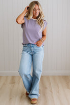 Woman wearing a striped shirt and jeans standing against a white paneled wall.