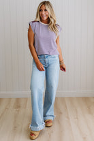 Woman wearing a striped shirt and light blue jeans standing against a white paneled wall.