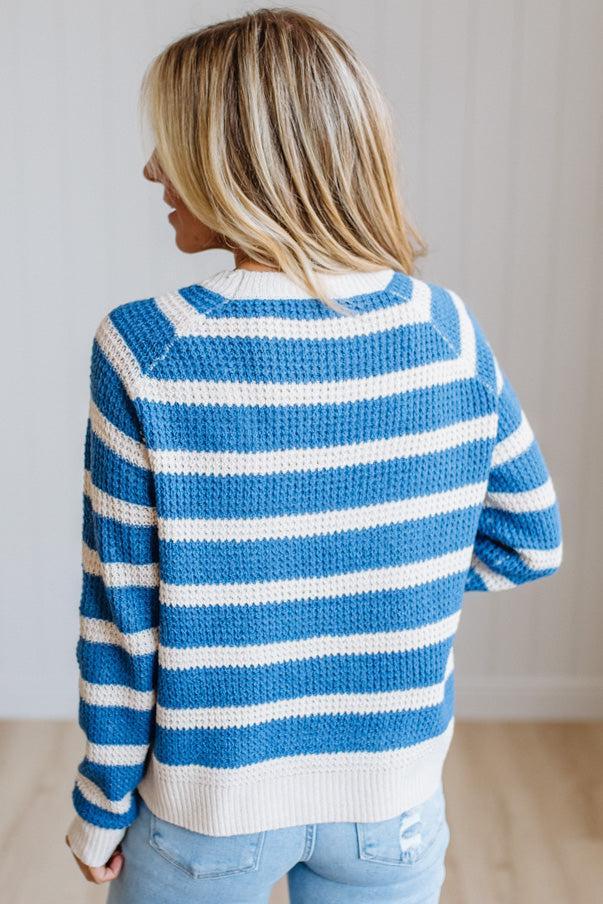 A woman shown from behind wearing a blue and white horizontally striped knit sweater and light blue jeans in a bright indoor setting.