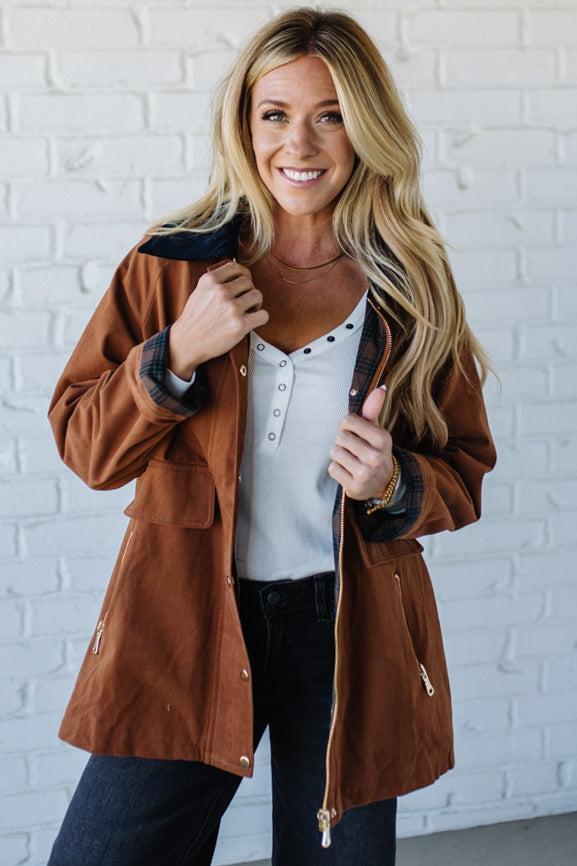 Woman wearing a brown jacket over a white shirt with a white brick wall background