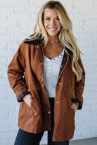 Woman wearing a brown jacket over a white shirt with a brick wall background