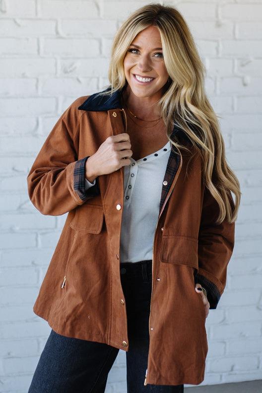 Woman wearing a brown jacket against a white brick wall