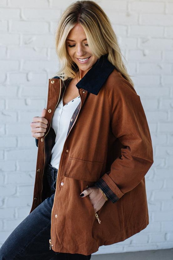 Woman wearing a brown jacket with a white brick wall background