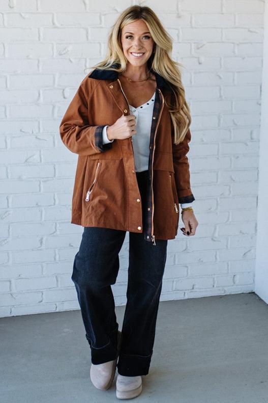 Woman wearing a brown jacket with a white brick wall background