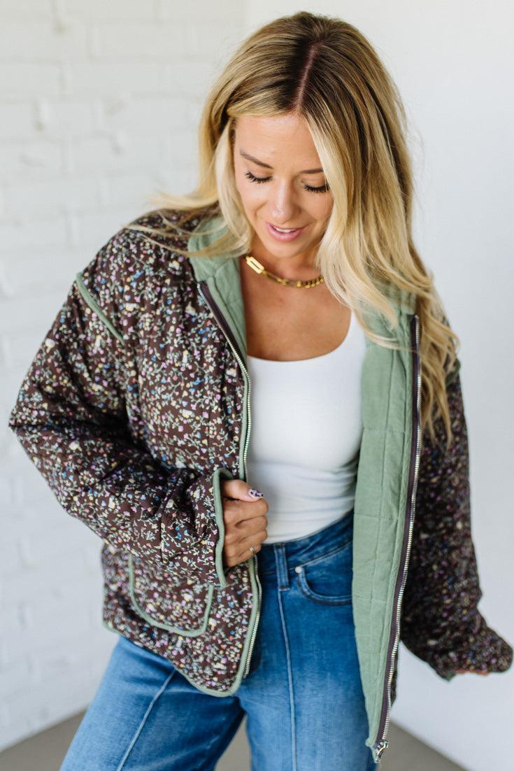 Woman wearing a floral jacket over a white top and blue jeans against a white wall.