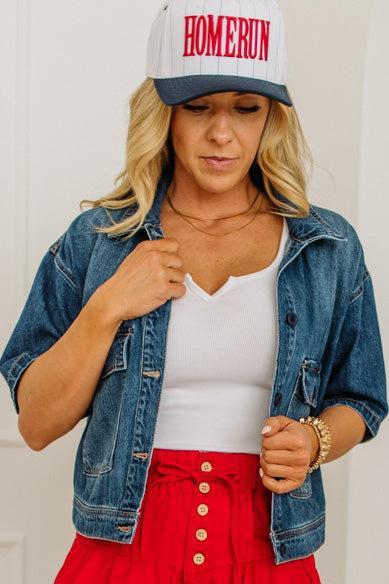 Woman wearing a denim jacket, white top, red skirt, and 'HOMERUN' cap.