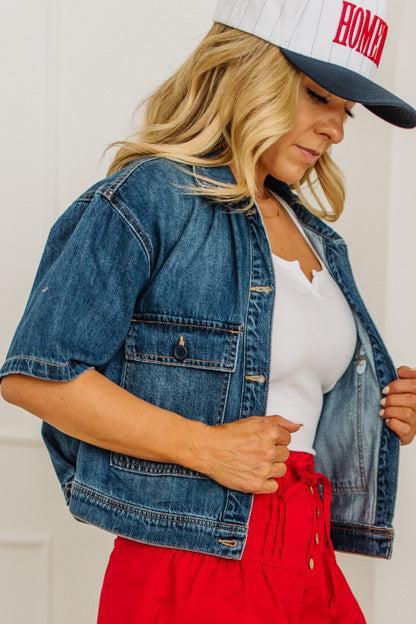 Woman wearing a denim jacket, white top, red pants, and a cap with 'HOME' text.