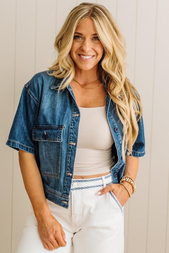 Woman wearing a denim jacket over a white top and pants, standing against a light background