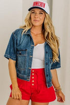 Woman wearing a denim jacket, white top, red shorts, and a 'Homerun' cap.