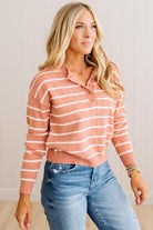 A woman wearing a long-sleeve knit polo-style sweater with horizontal peach and white stripes, paired with blue jeans, standing against a light paneled wall.