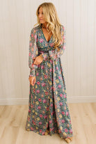 Woman wearing a floral dress standing against a white paneled wall.