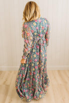 Woman wearing a floral dress standing against a wooden paneled wall.