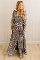Woman wearing a floral dress standing against a white paneled wall.