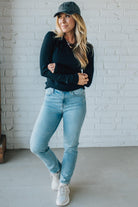 Woman wearing a black sweater, light blue jeans, and white sneakers against a white brick wall.