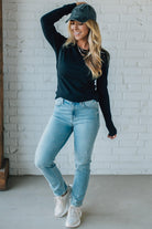 Woman wearing a black top, light blue jeans, and white sneakers against a white brick wall.