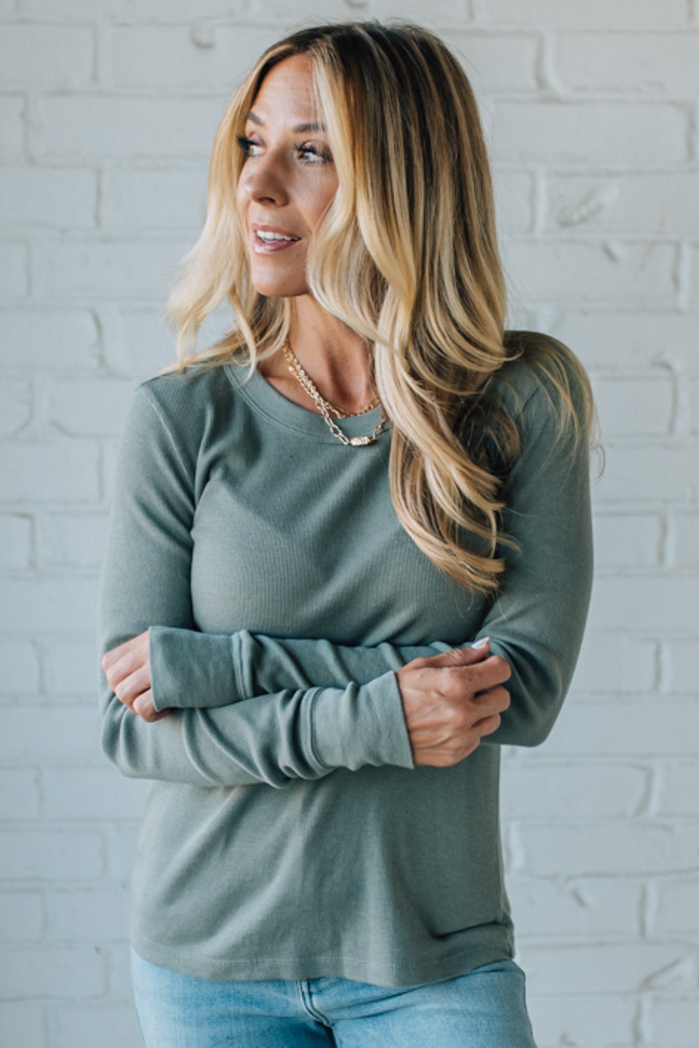 Woman wearing a green long-sleeve top against a white brick wall