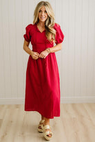 Woman wearing a red dress standing against a white paneled wall.