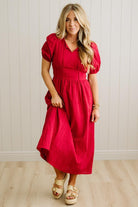 Woman wearing a red dress standing against a white paneled wall.