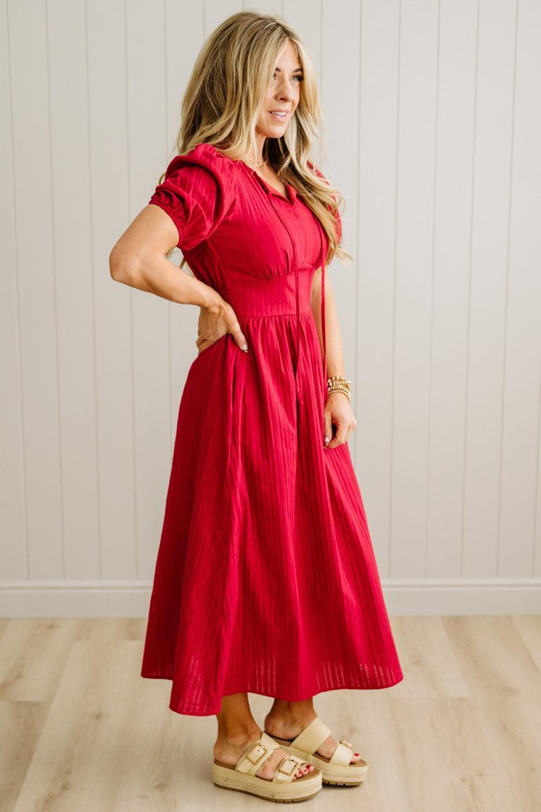 Woman wearing a red dress standing against a white paneled wall.