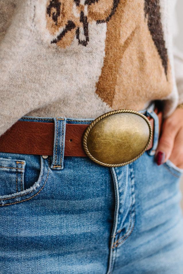 Close up image of a woman in blue jeans and patterned sweater featuring a Western Oval Buckle Leather Belt.